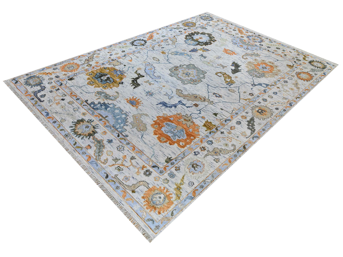 Oushak-style rug in light blue with central medallion, floral motifs, orange and dark teal accents