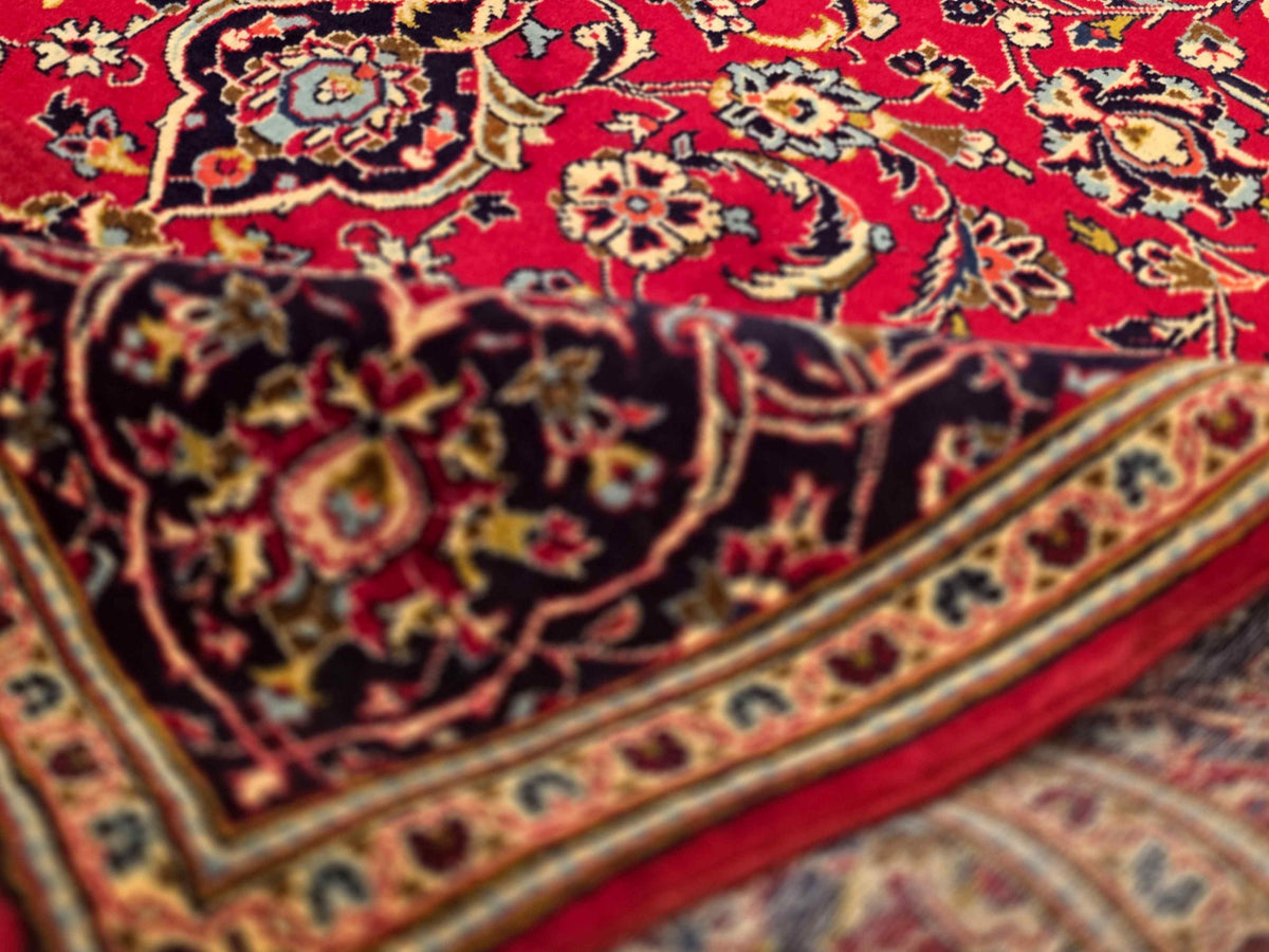 Kashan rug close-up, red floral pattern with navy border and gold trim