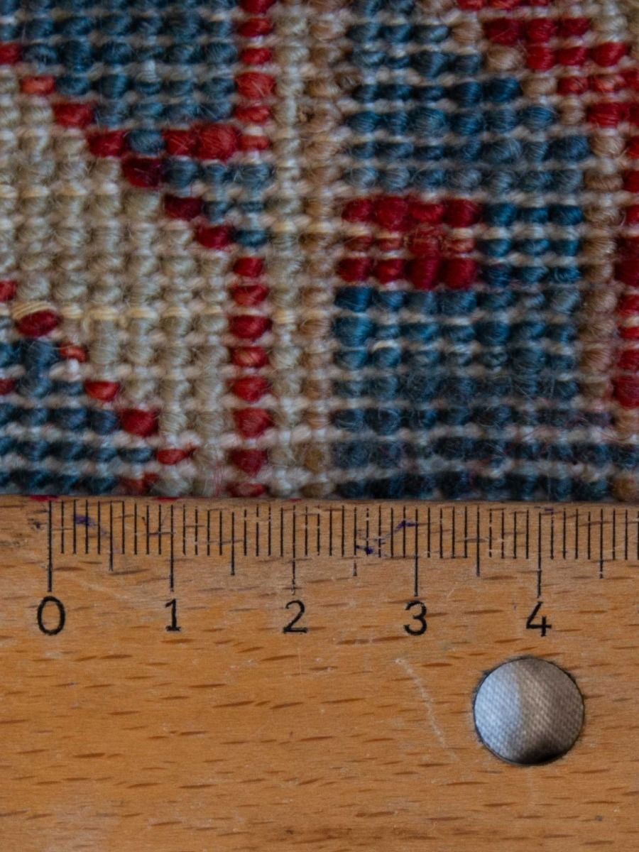 Close-up of rug fibers in cream, blue and red with small grid texture