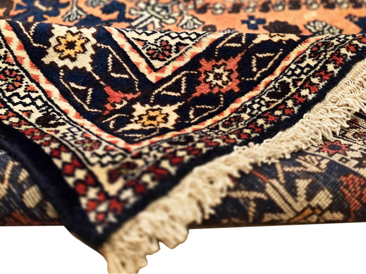 Close-up rug corner with dark navy and orange geometric design and cream fringe