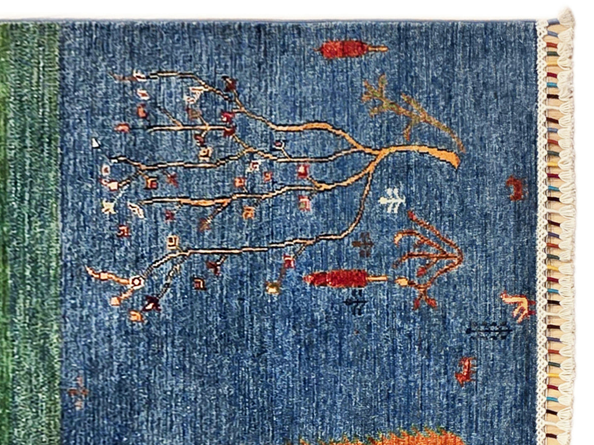 Close-up of blue rug with multicolor tree branches and beige fringe on the edge.