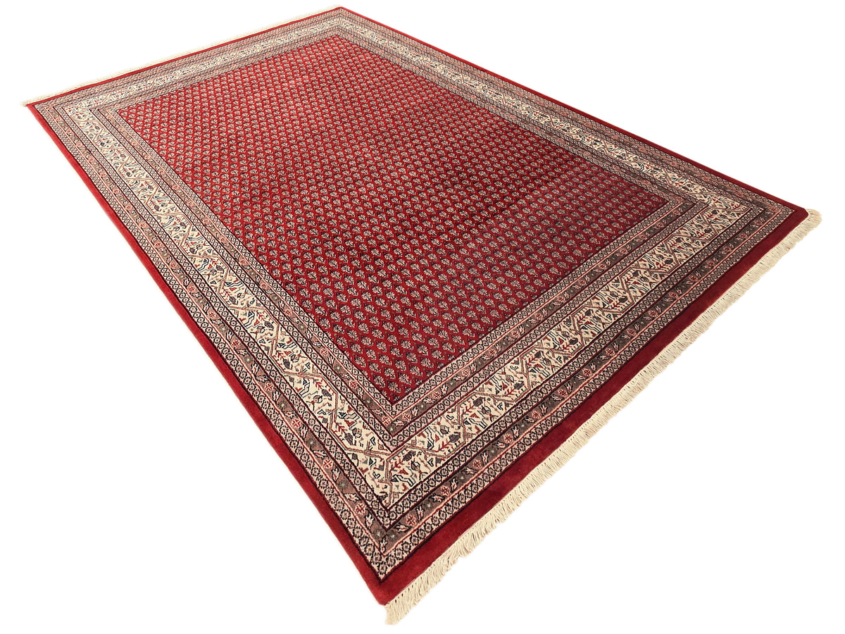Red area rug with geometric diamond pattern and cream border trim, fringed ends.