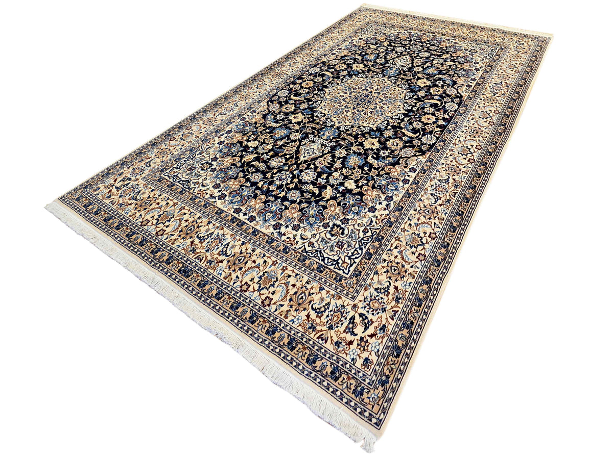 Nain rug shown diagonally with navy floral medallion, cream outer border, fringe edge.