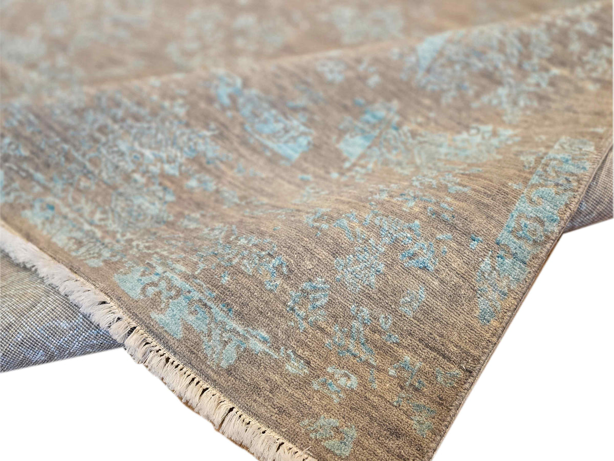 Modern area rug edge with short fringe; tan and muted blue distressed pattern