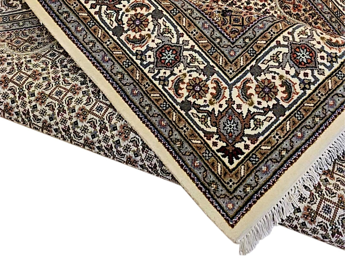 Oriental rug border detail with cream backdrop, dark blue stripes, floral corner motifs, fringe