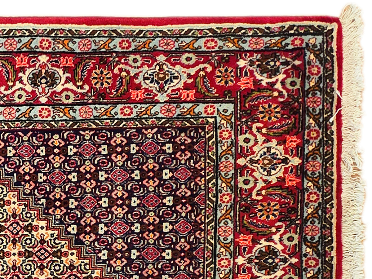 Rug corner with red, navy, and cream intricate motifs and cream fringe edge