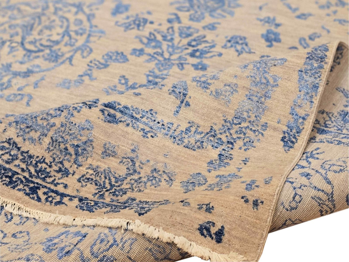 Rug edge close-up showing blue pattern on beige field and thin fringe along border.
