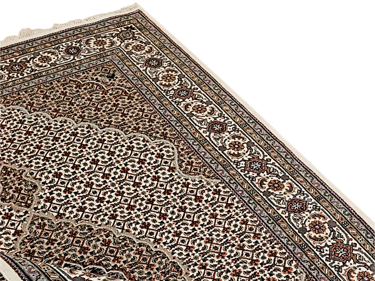 Corner view of patterned area rug with dark border lines and ornate floral motifs.