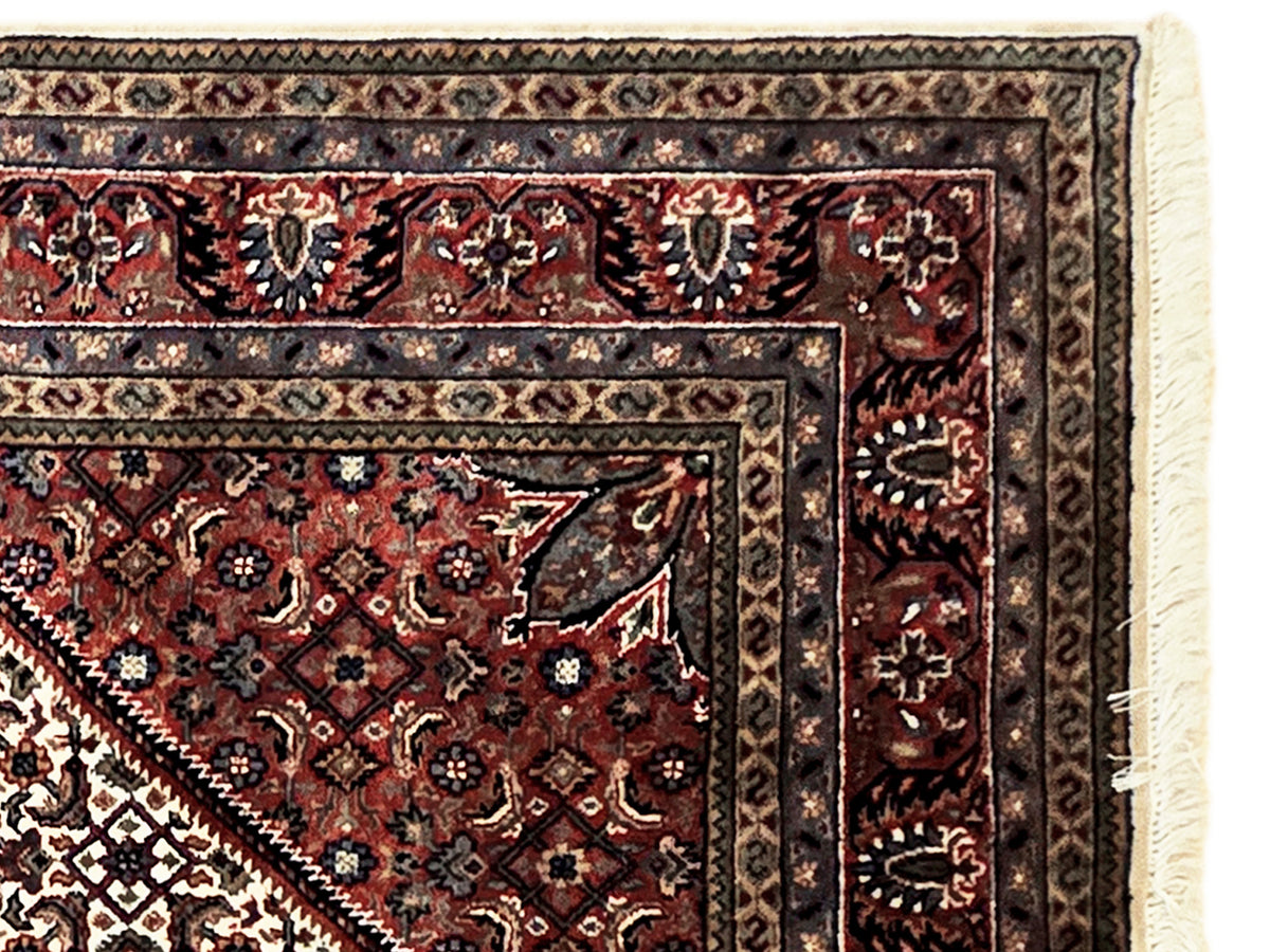 Rug border detail with dark navy, rust, and cream motifs and fringed edge.