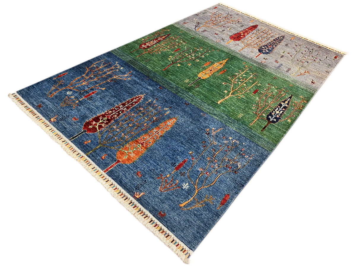 Diamond view of blue, green, and gray rug with tree and bird motifs, fringed edges.